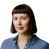 Portrait of Karolina on a grey background. She's slightly smiling, looking into the camera, wearing a light blue shirt.